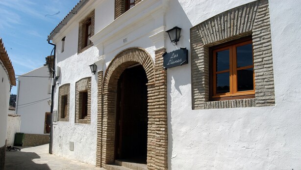 A building with a white facade, a large arched doorway, and a sign reading "Los Llanos." - TUGASA Hotel La Posada (Villaluenga del Rosario)