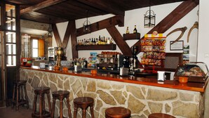 A bar with wooden stools, stone walls, and a variety of bottles and snacks. - TUGASA Hotel La Posada (Villaluenga del Rosario)