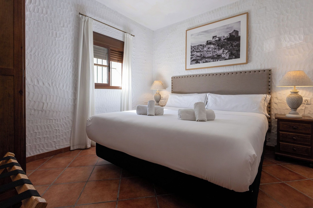 Habitación de hotel con una cama grande, dos lámparas de noche, un cuadro enmarcado en la pared y una ventana con cortinas.