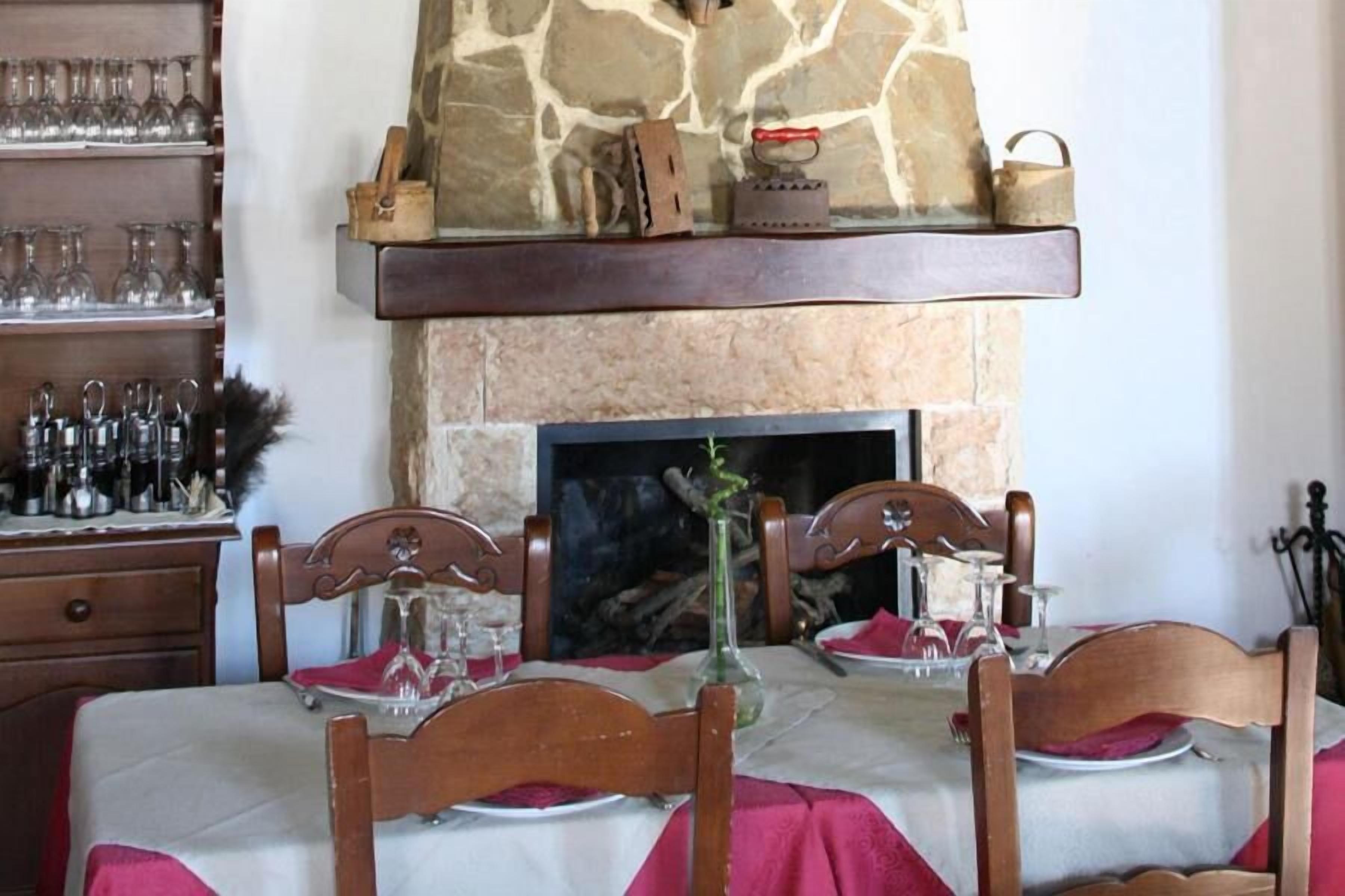 A dining area with a stone fireplace, wooden chairs, and a table set for two.
