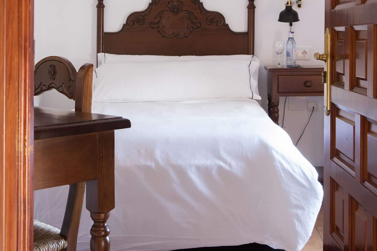 A neatly made bed with a wooden headboard, a bedside table with a lamp, and a chair.