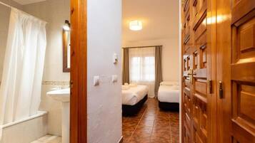 A hotel room with a bathroom, a bed, a bedside table, and a window with curtains.