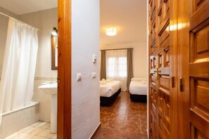 A hotel room with a bathroom, a bed, a bedside table, and a window with curtains. - Las Truchas (El Bosque)