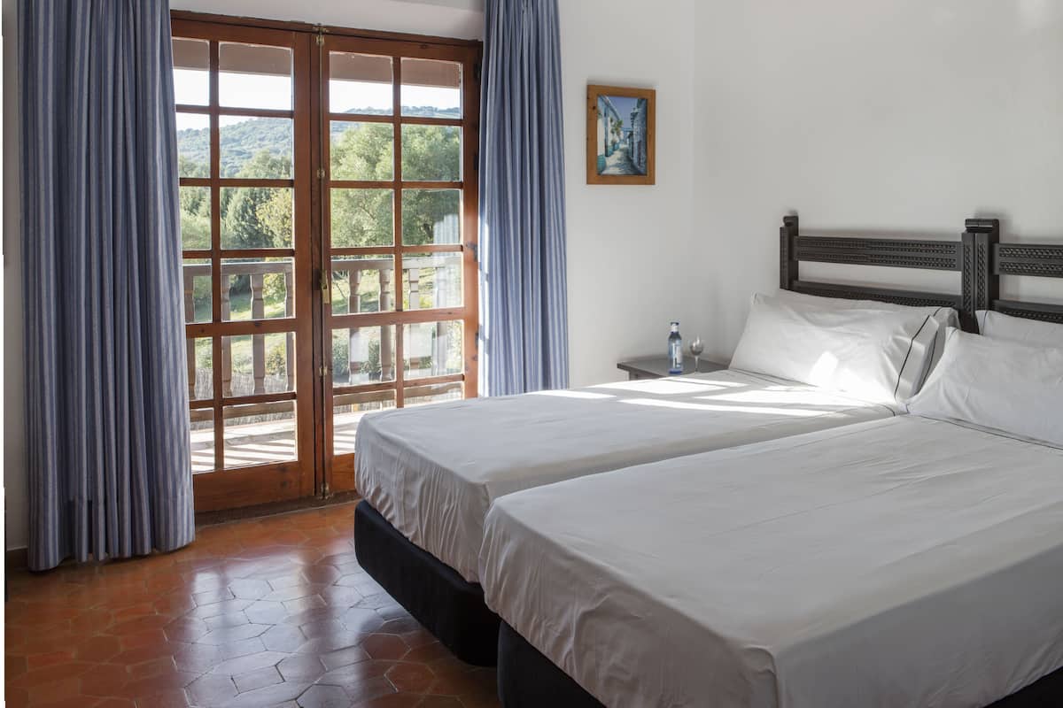 A bedroom with two beds, a wooden headboard, a nightstand with a bottle and glass, and a painting on the wall.