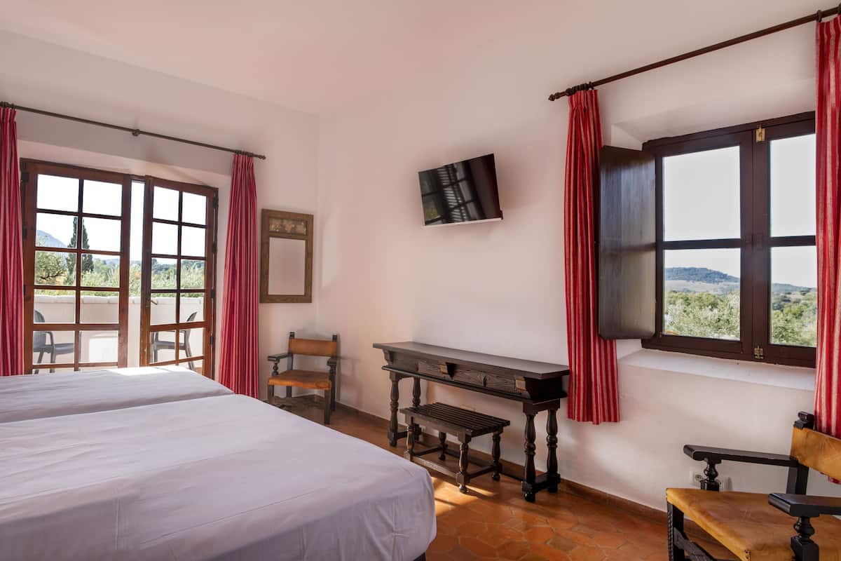 A room with two beds, a wooden desk, a chair, a TV, and a window with curtains.