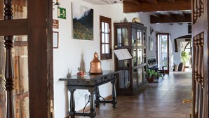 Un pasillo amplio con vigas de madera y una araña, que conduce a una sala con un piano y un aparador.