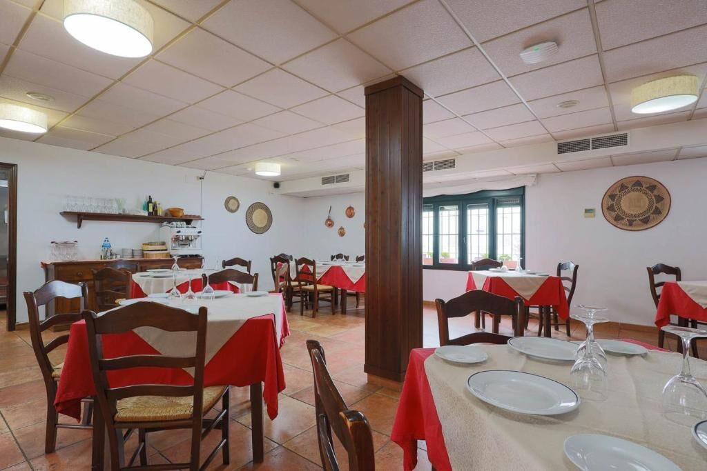 A dining area with tables set for service, chairs, and a kitchen area in the background.