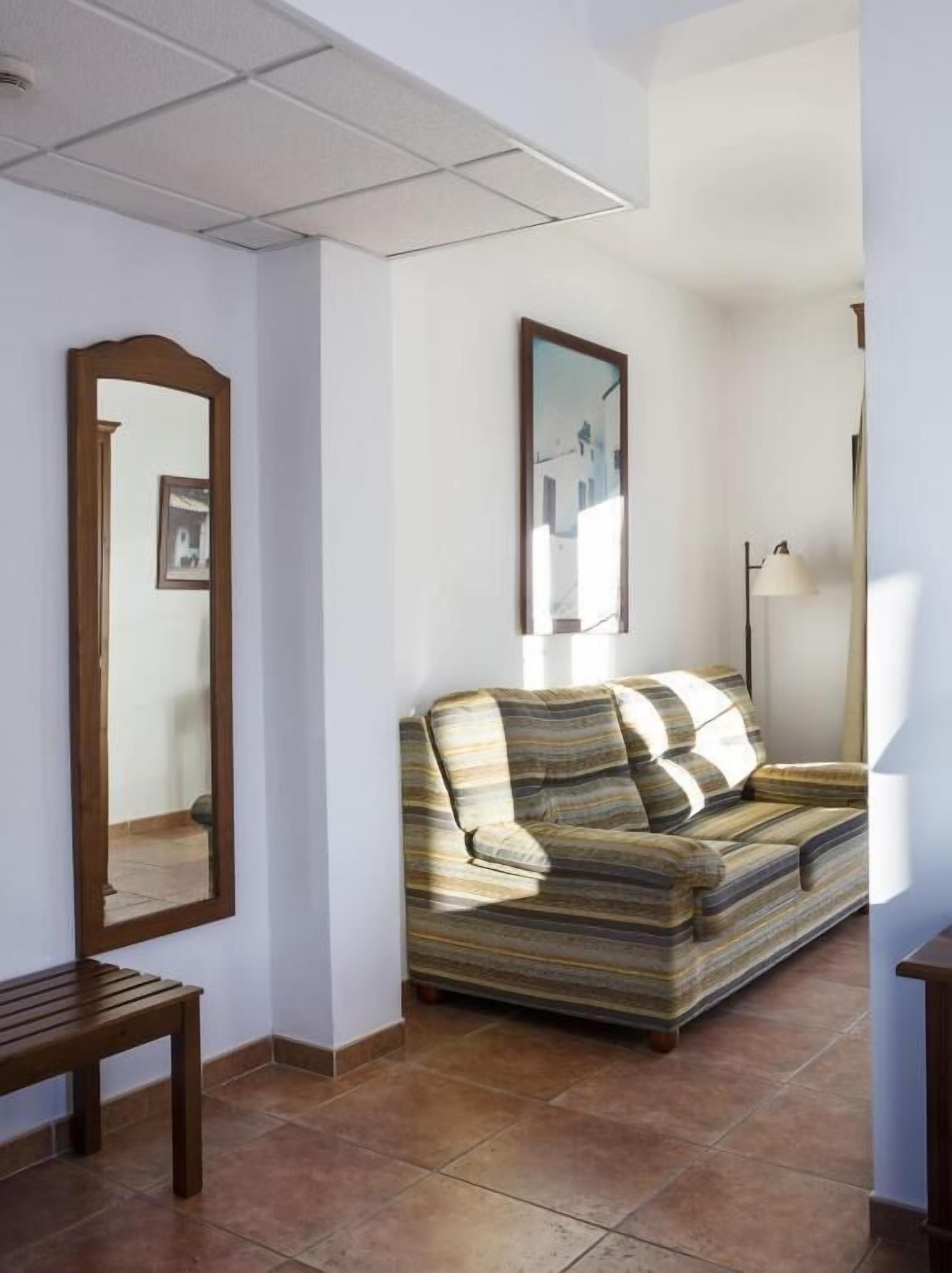 A living room with a sofa, a wooden bench, a floor lamp, and a mirror on the wall.
