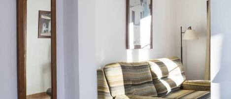 A living room with a sofa, a wooden bench, a floor lamp, and a mirror on the wall.