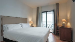 A hotel room with a large bed, two bedside lamps, a wooden nightstand, a view of the outside balcony, and a door leading to the balcony. - TUGASA Sierra Y Cal (Olvera)