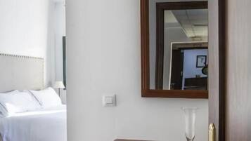 Una habitación de hotel con una cama, una mesita de noche con un vaso y un espejo en la pared.