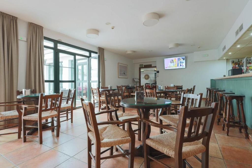 Un comedor amplio con varias mesas y sillas, una barra y ventanas grandes que dejan entrar luz natural.
