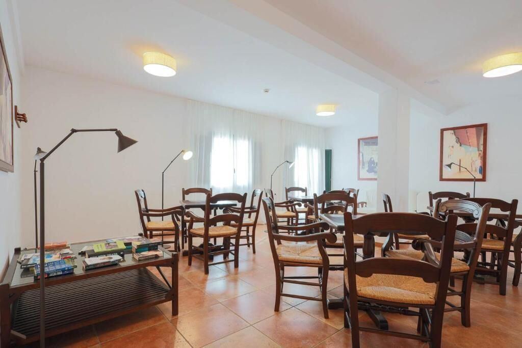 A room with multiple wooden chairs and tables, a standing lamp, and a bookshelf with books.
