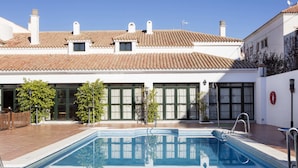 A swimming pool with a tiled deck, surrounded by a building with a tiled roof and large windows. - TUGASA Sierra Y Cal (Olvera)