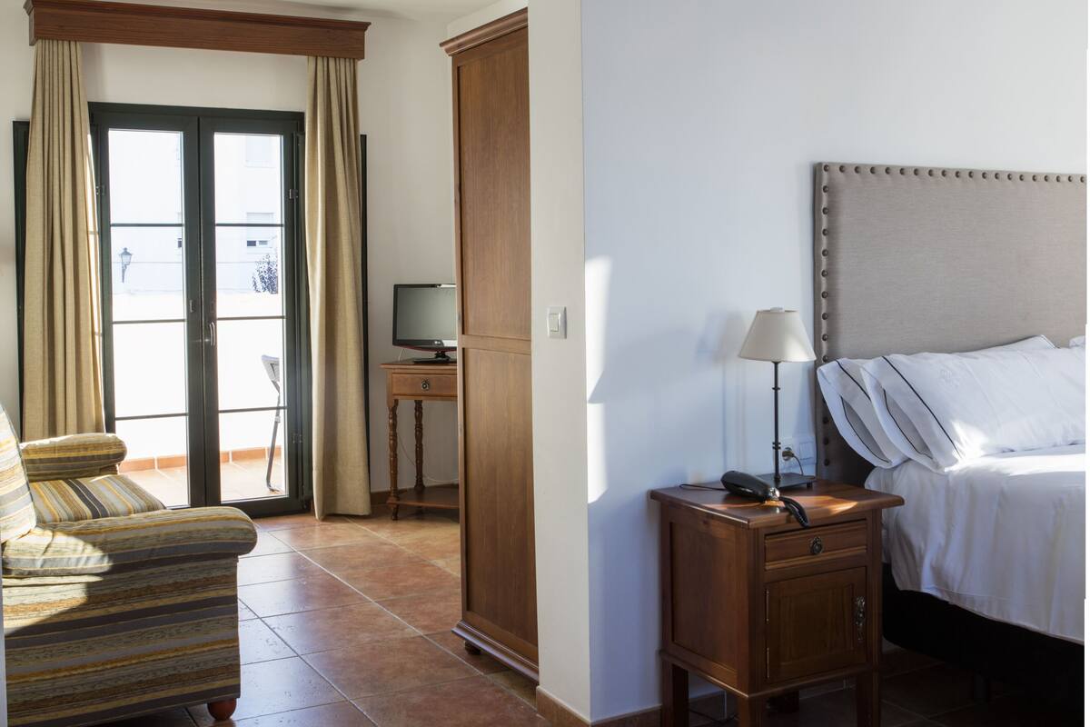 A hotel room with a bed, bedside table, lamp, and a sofa.