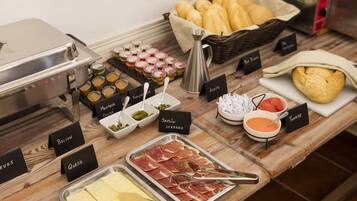 Una mesa de buffet con diversos alimentos etiquetados, incluyendo carnes, quesos y salsas.