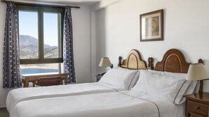 Uma cama de casal com cabeceira de madeira, duas mesas de cabeceira com luminárias, uma janela com cortinas e um quadro na parede.