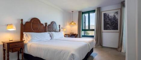 Een hotelkamer met een groot bed, nachtkastjes, een raam met gordijnen en een ingelijst kunstwerk aan de muur.