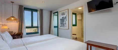 Habitación de hotel con una cama grande, televisor montado en la pared y una ventana con cortinas.