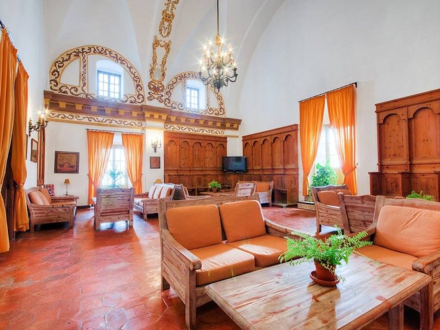 Una habitación amplia con muebles de madera, un candelabro y ventanas grandes con cortinas.