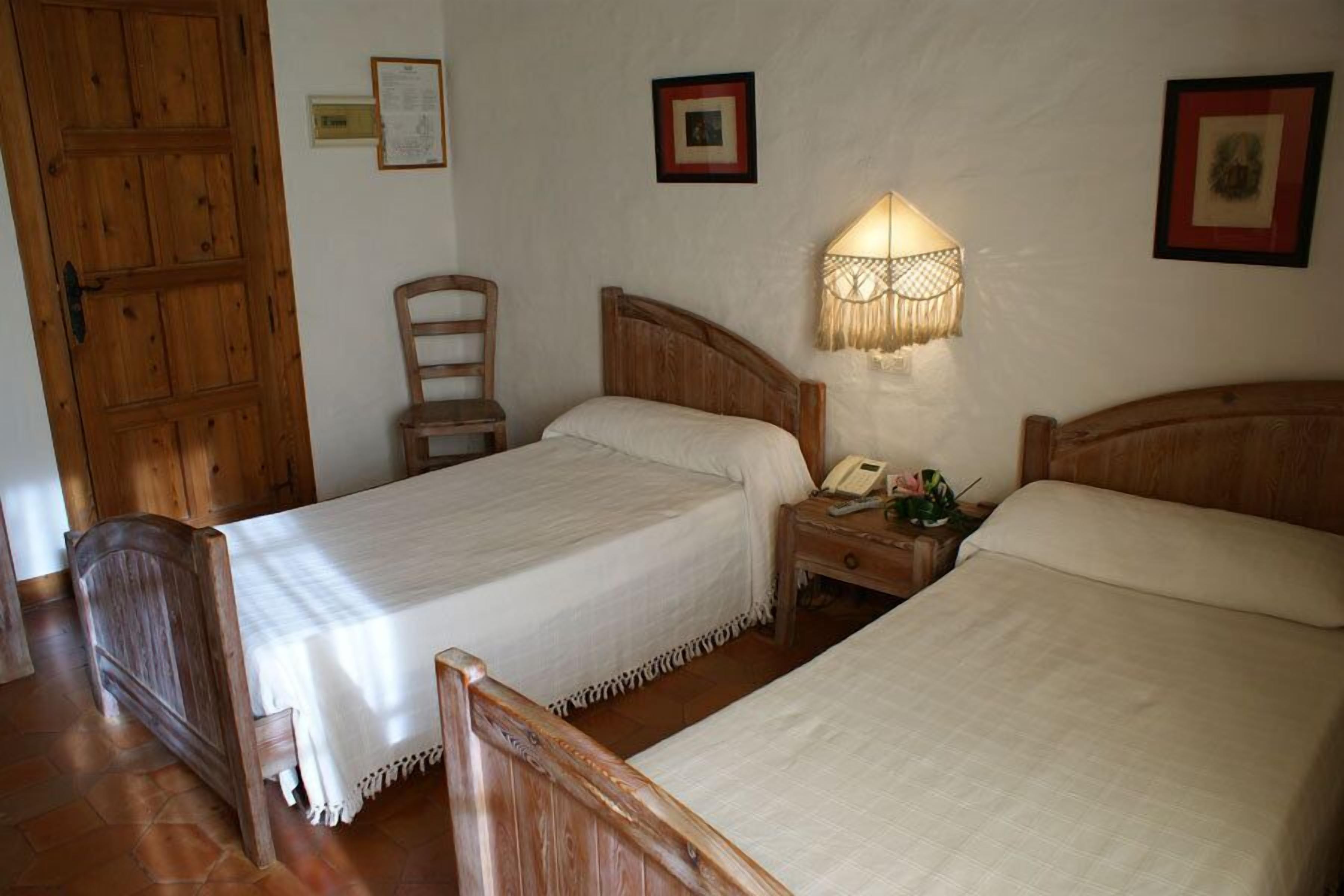 A room with two wooden beds, a wooden chair, a nightstand with a lamp, and a wooden door.