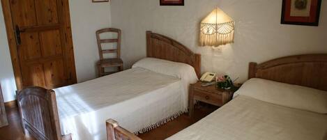 A room with two wooden beds, a wooden chair, a nightstand with a lamp, and a wooden door.