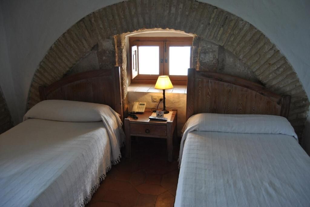 A bedroom with two beds, a nightstand with a lamp, and a window with a view.
