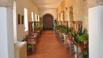 A corridor with a brick archway, wooden benches, potted plants, and a tiled floor.