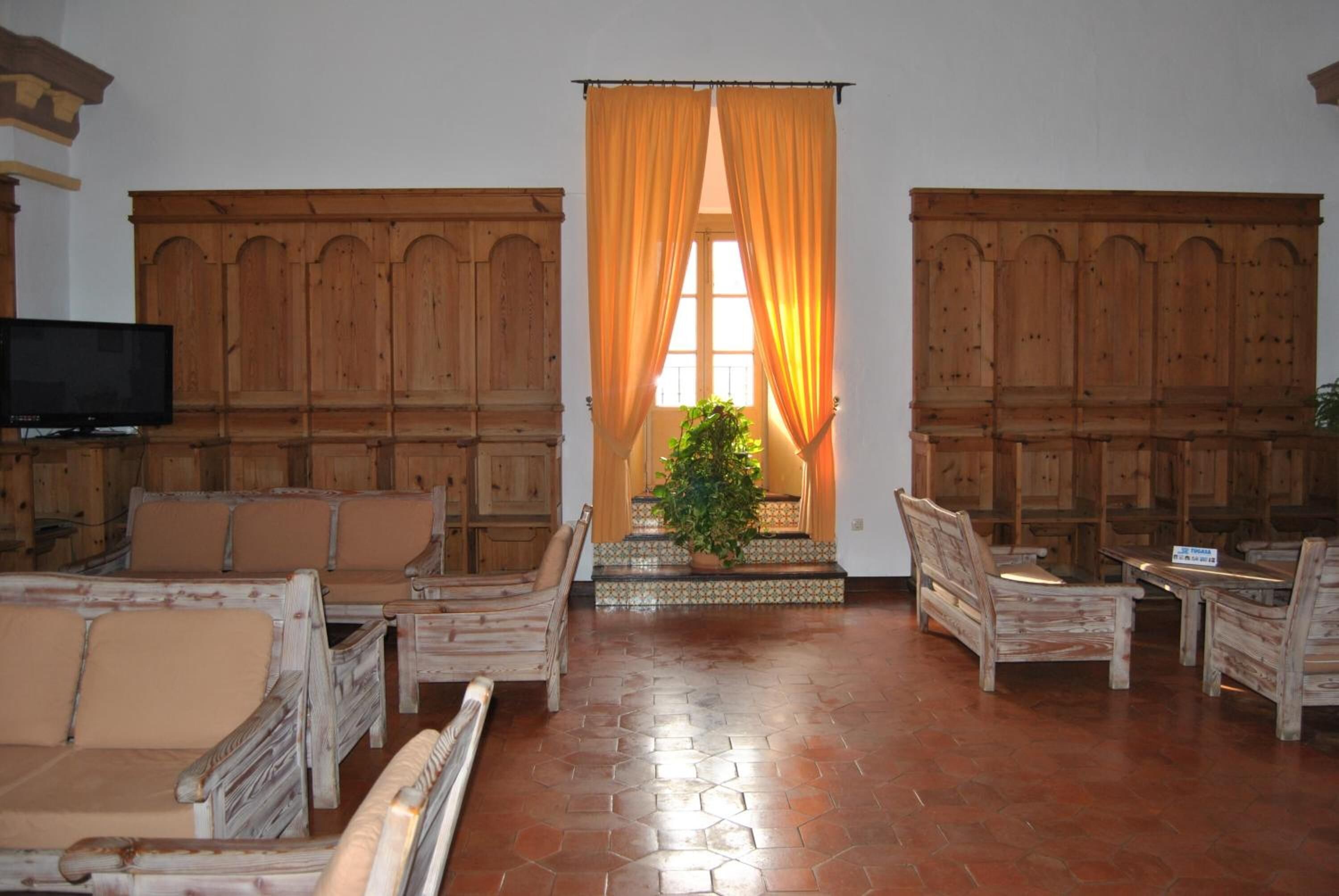 A room with wooden furniture, a television, and a plant near a window with curtains.