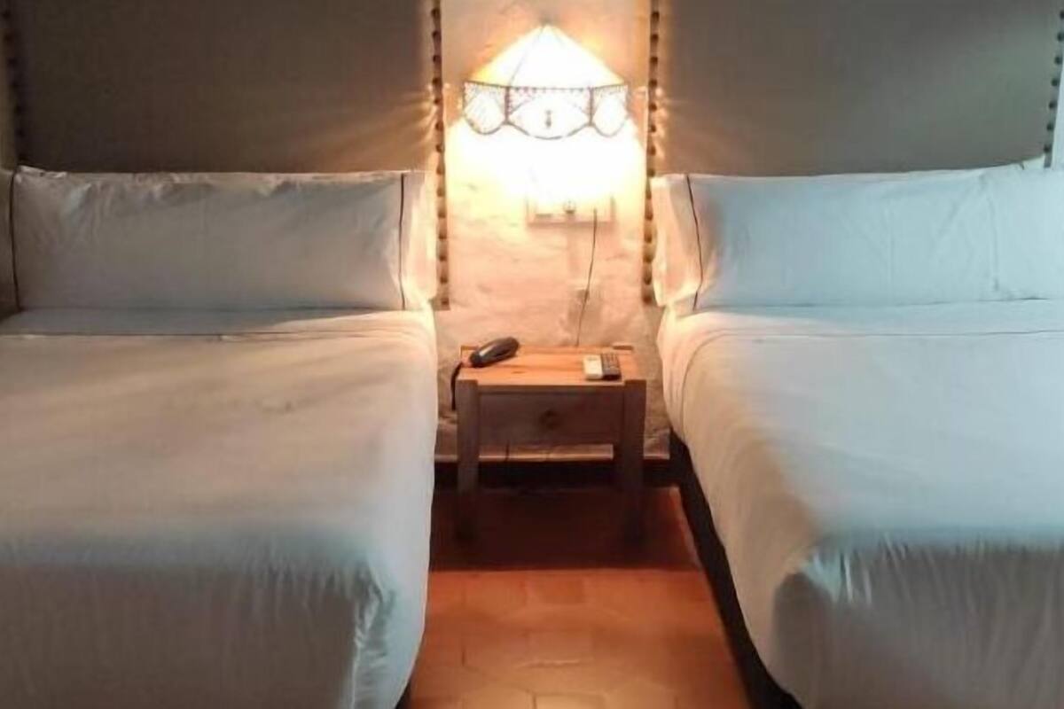 A room with two single beds, a nightstand with a lamp, and a window with curtains.