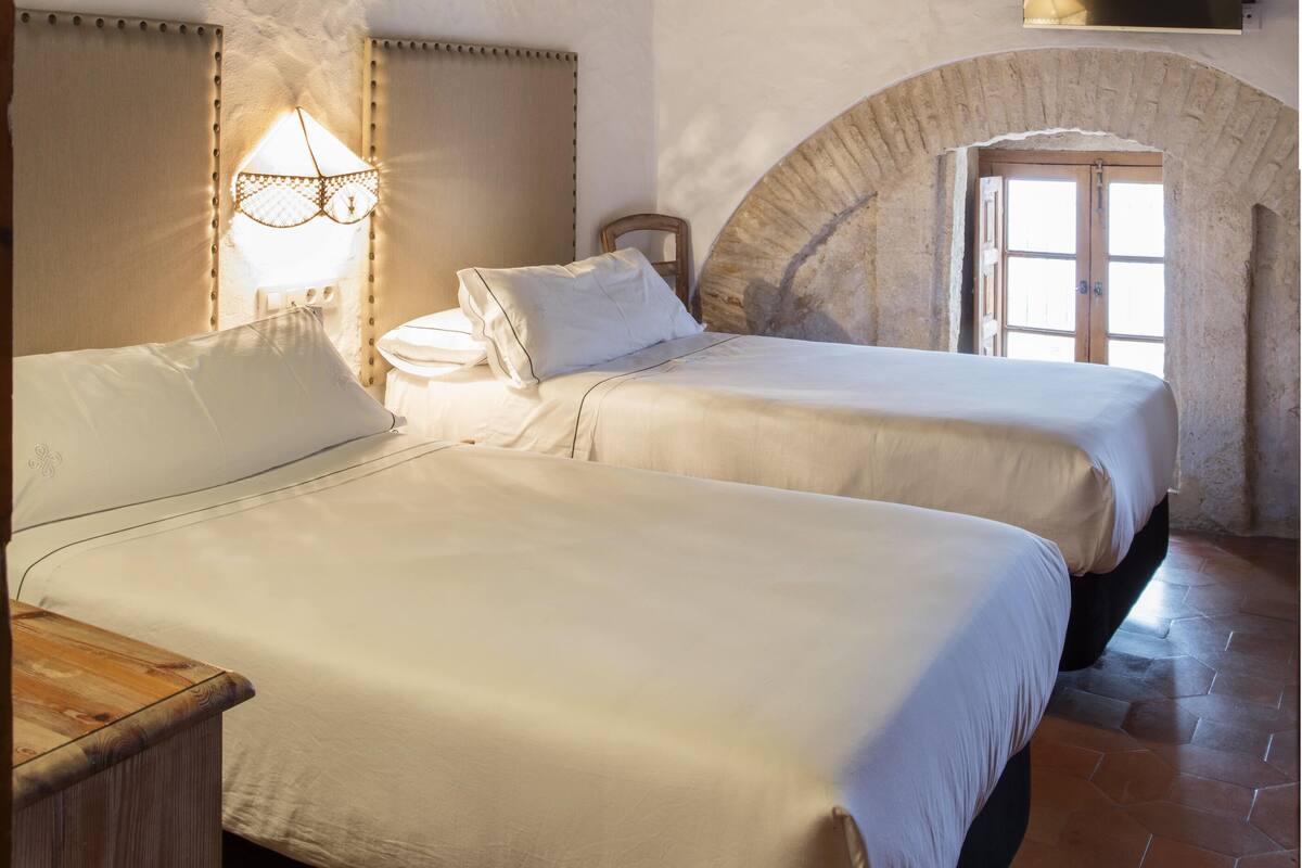 A bedroom with two beds, a wooden ceiling, a stone wall, and a TV mounted on the wall.