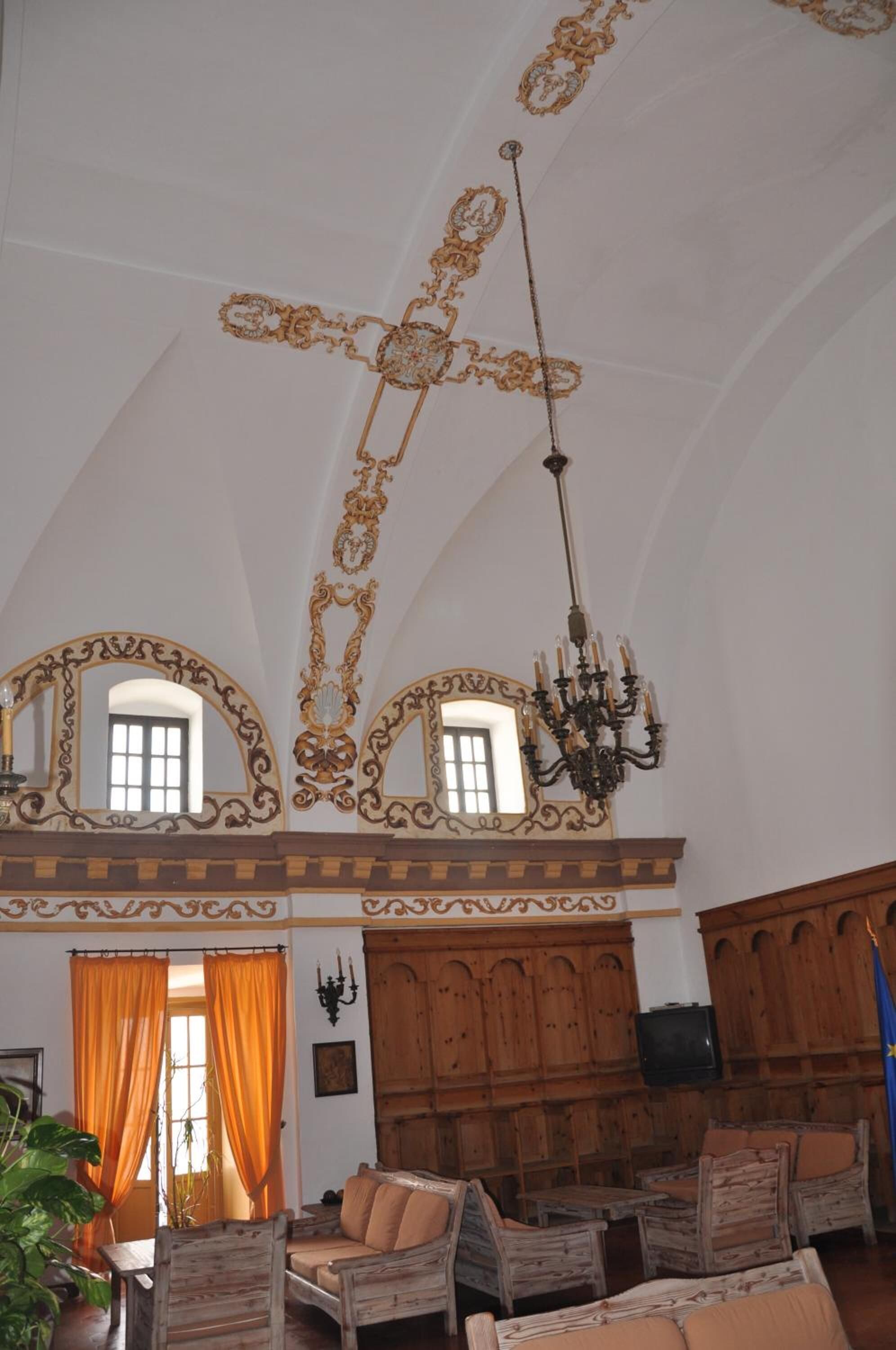 A room with a high arched ceiling, ornate gold detailing, a chandelier, wooden furniture, and a television.