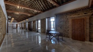 A spacious corridor with a polished floor, wooden ceiling beams, stone walls, and large windows. - TUGASA Convento San Francisco (Vejer de la Frontera)