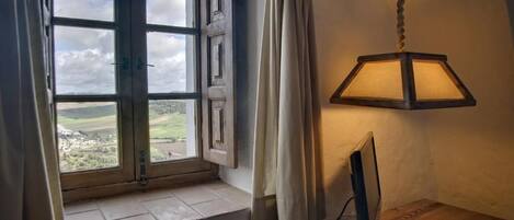 Una habitación con un ventanal grande, un escritorio de madera y una lámpara colgante.