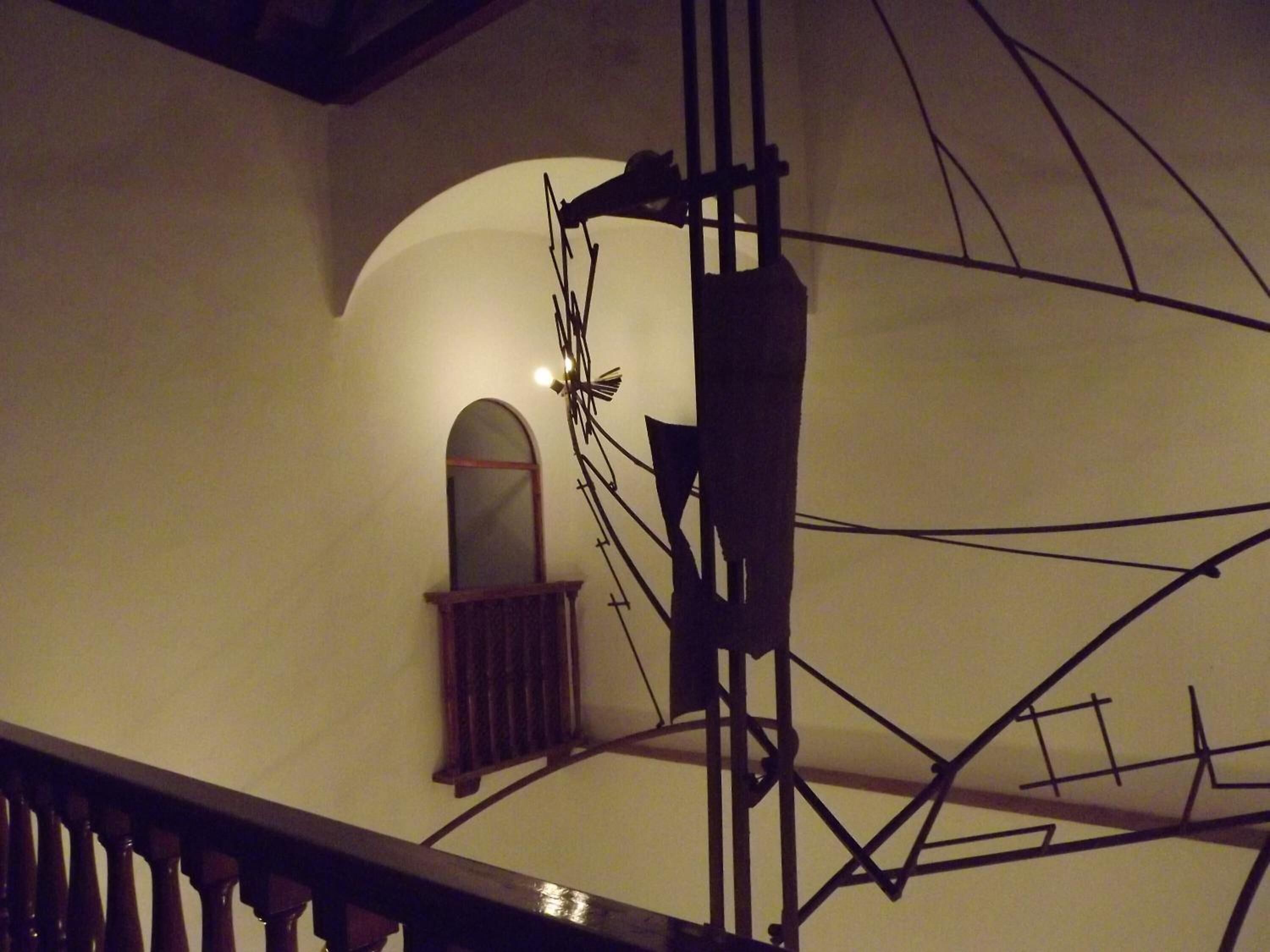 A staircase with a wooden handrail and a wall with a window and electrical wires.