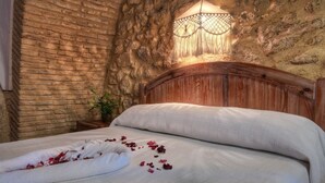 A bed with a white blanket and rose petals, a wooden headboard, and a stone wall. - TUGASA Convento San Francisco (Vejer de la Frontera)