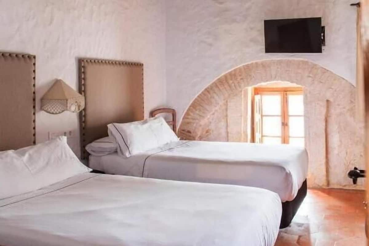 A bedroom with two beds, a stone wall, wooden beams, a TV, and a window with a view.