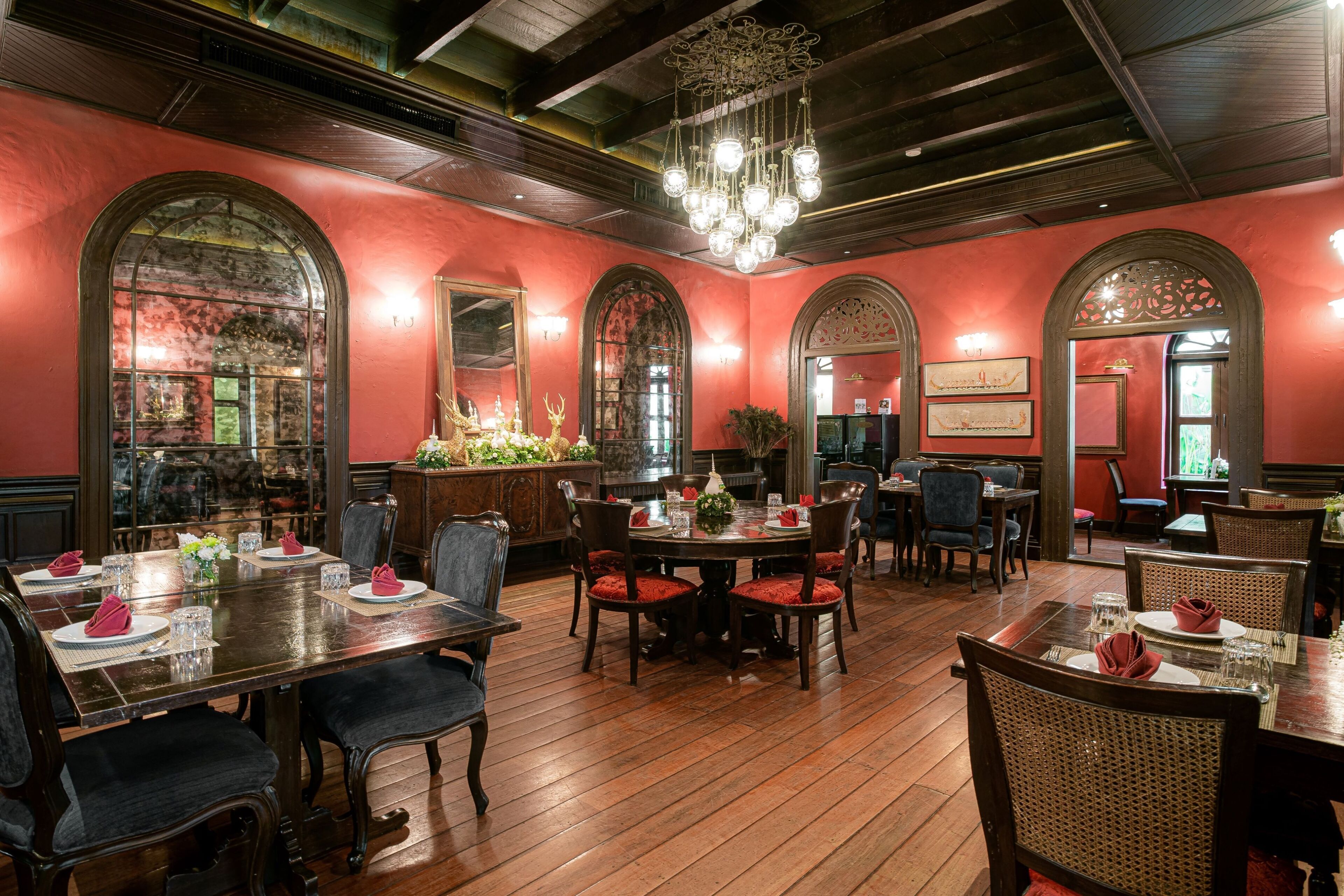 A dining area with wooden tables and chairs, red walls, and a chandelier.