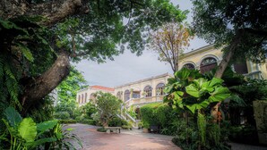 A courtyard with a paved walkway, lush greenery, and a building with arched windows and balconies. - Praya Palazzo (Bangkok)