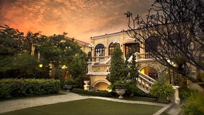 A grand building with a central staircase, surrounded by lush greenery and well-manicured lawns. - Praya Palazzo (Bangkok)