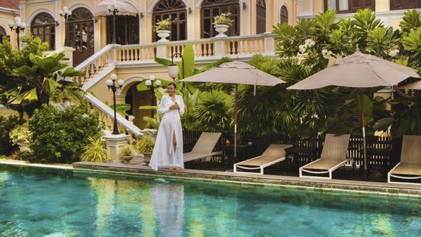 A pool area with lounge chairs and umbrellas, surrounded by lush greenery and a building with arched windows and a staircase. - Praya Palazzo (Bangkok)