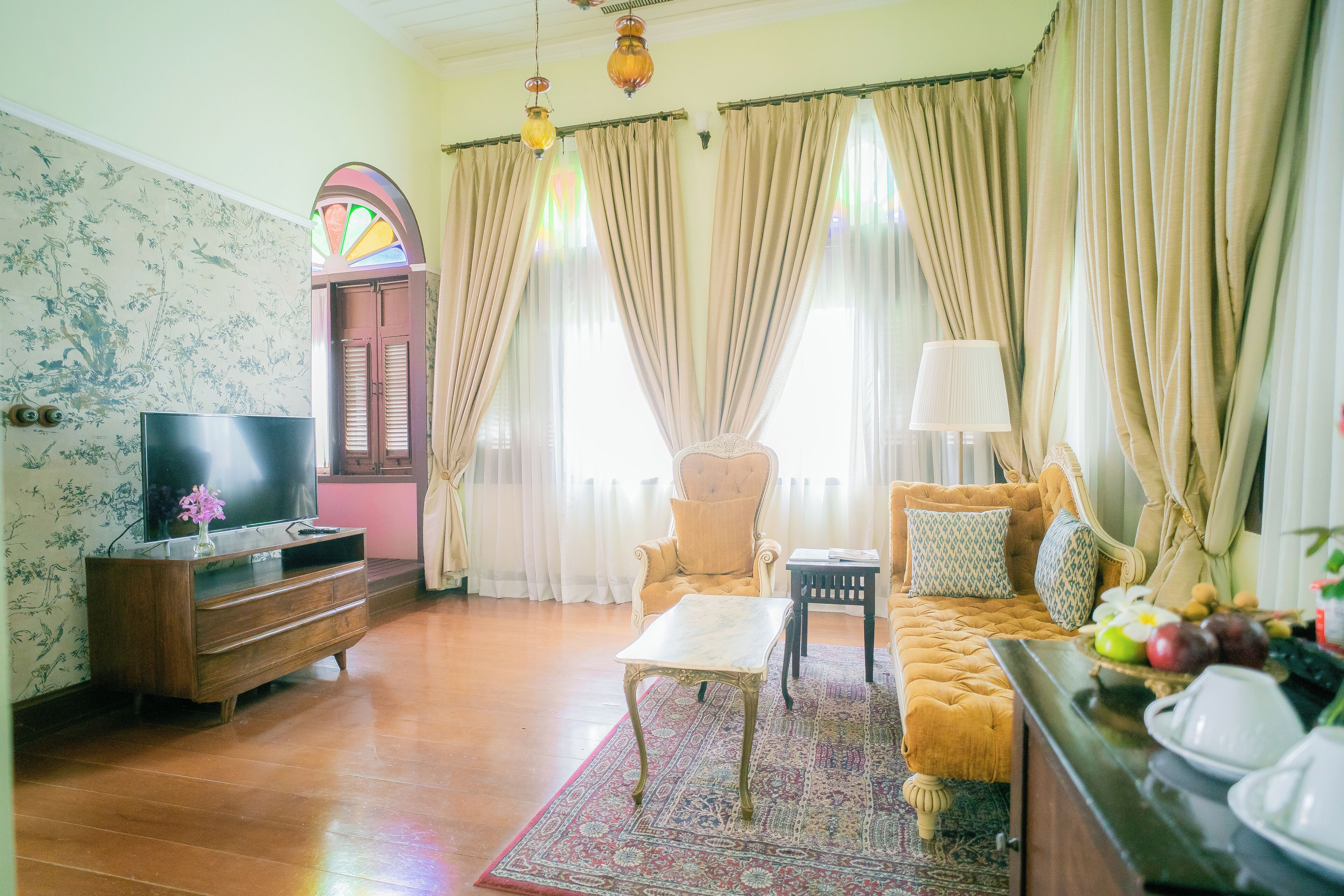 A living room with a sofa, armchair, TV, wooden cabinet, and a patterned rug.