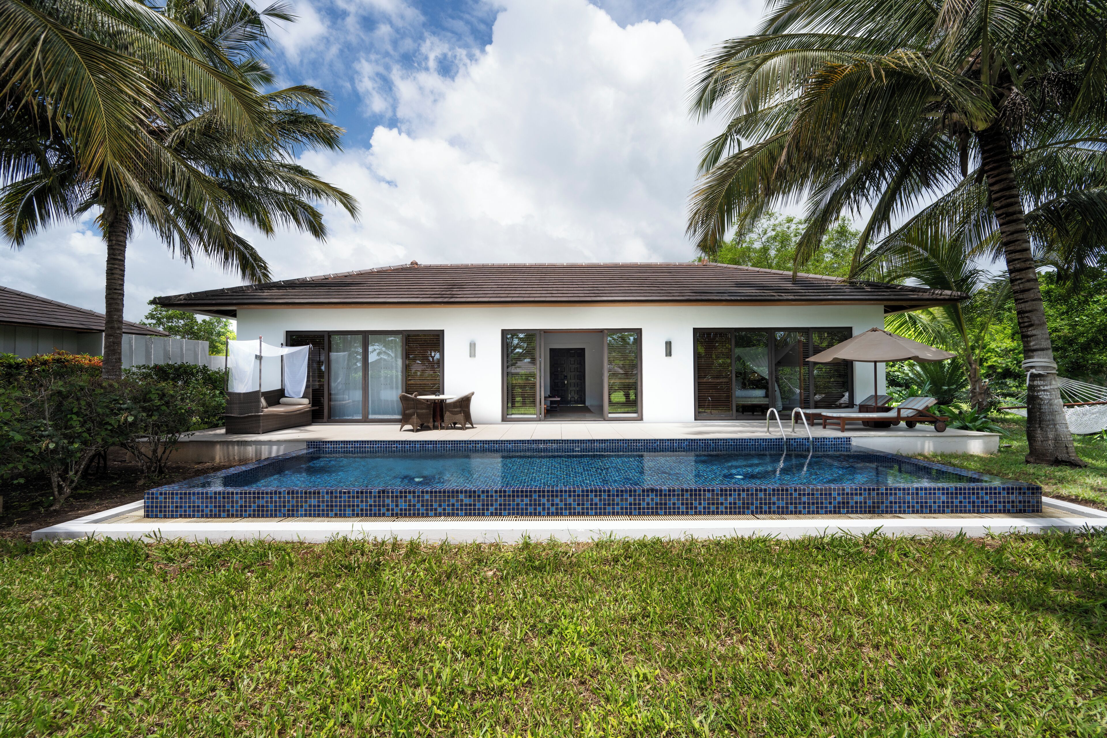 A modern house with a swimming pool, surrounded by palm trees and a well-maintained lawn.