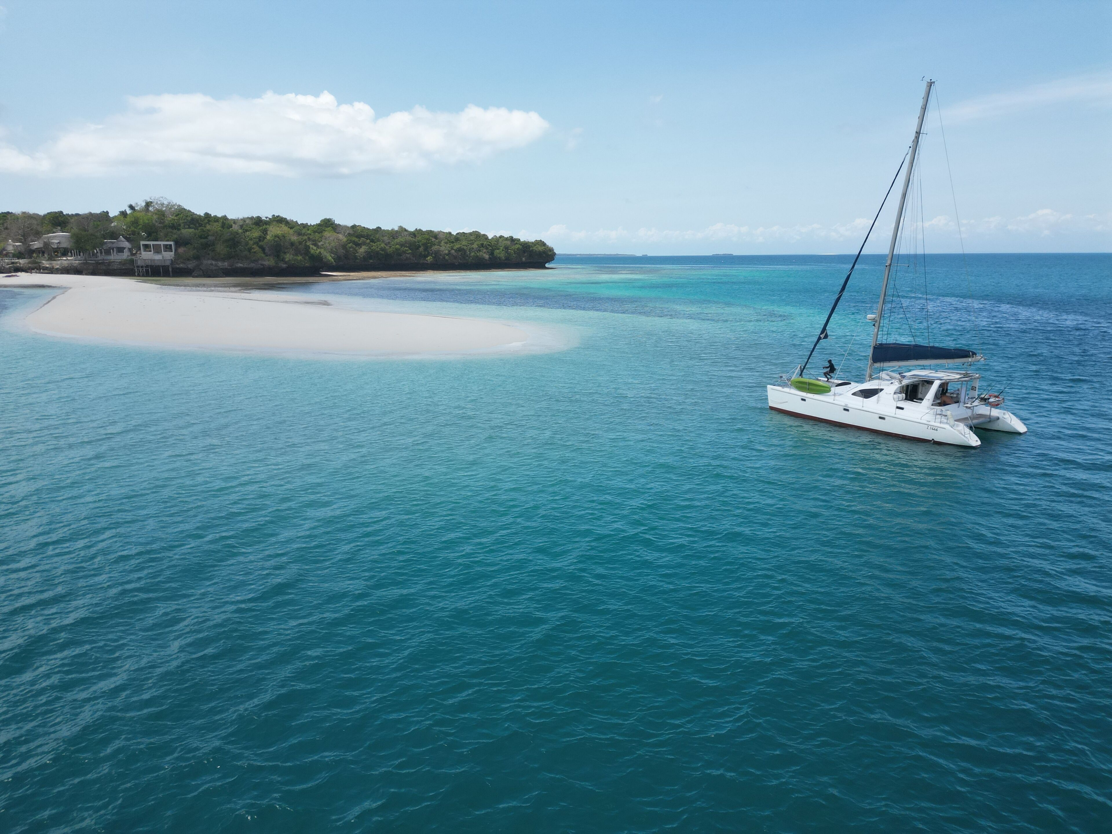 En vit yacht på turkosblått vatten, med en sandstrand och en skogbeklädd ö i bakgrunden.