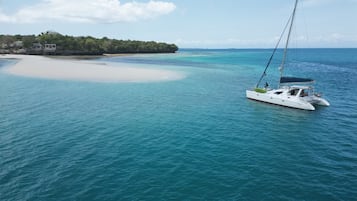 En vit yacht på turkosblått vatten, med en sandstrand och en skogbeklädd ö i bakgrunden.