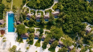 Vue aérienne d’un complexe hôtelier comprenant plusieurs villas, une piscine centrale et une végétation luxuriante environnante.