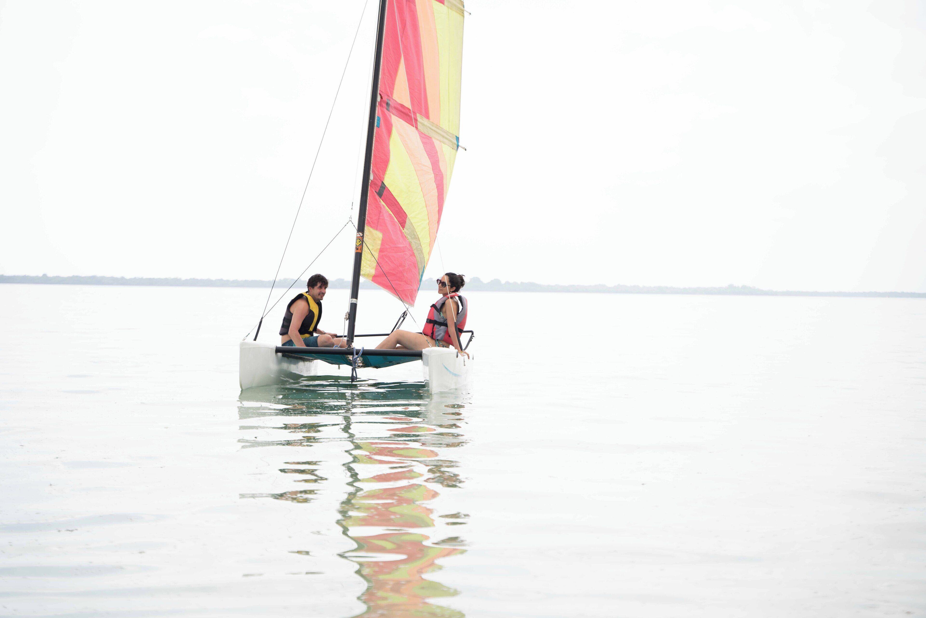 A sailboat with two people on board, floating on calm water.