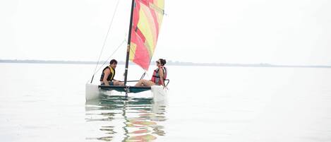 A sailboat with two people on board, floating on calm water.