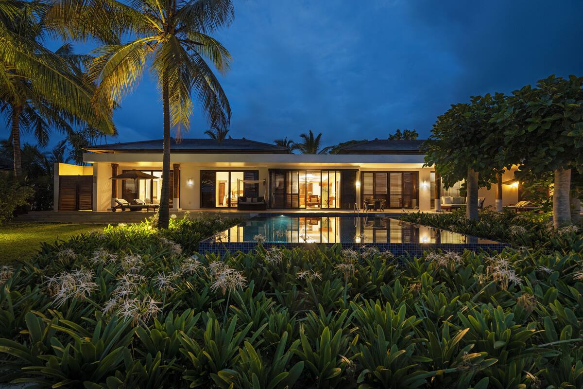 Ein modernes Haus mit Swimmingpool, umgeben von tropischer Bepflanzung.
