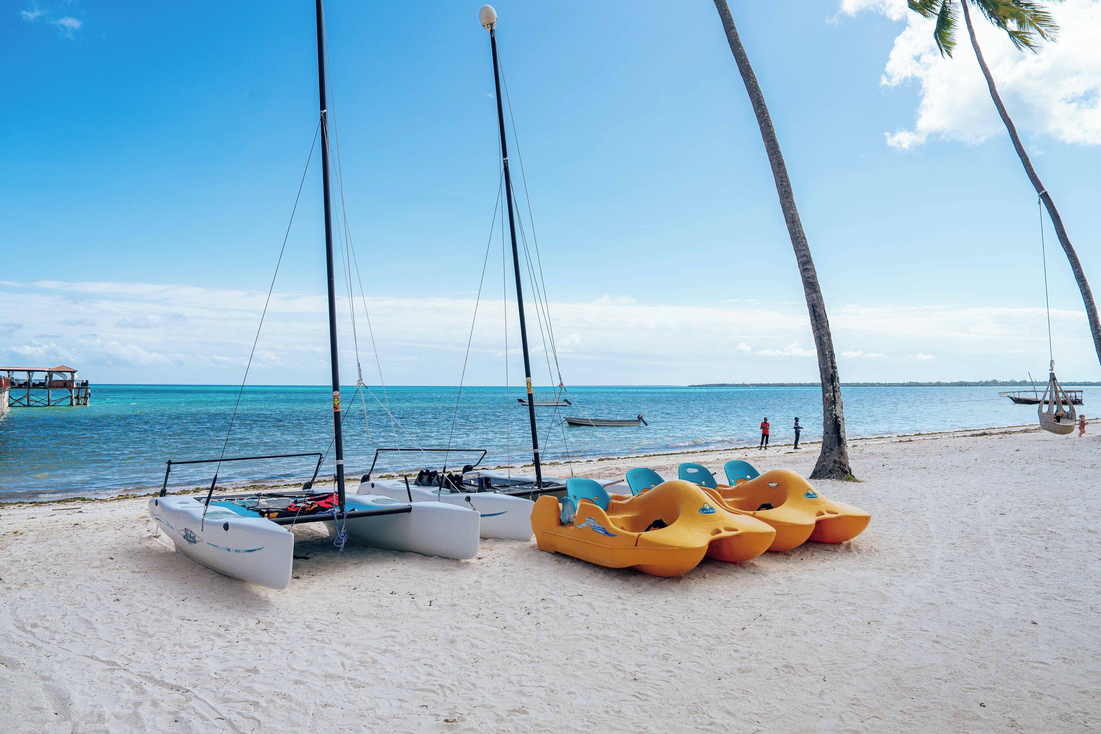 A beach with several boats and a wooden dock in the background.
